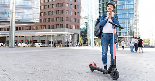 © tunedin / stock.adobe.com Frau mit E-Scooter setzt sich gerade einen Helm auf